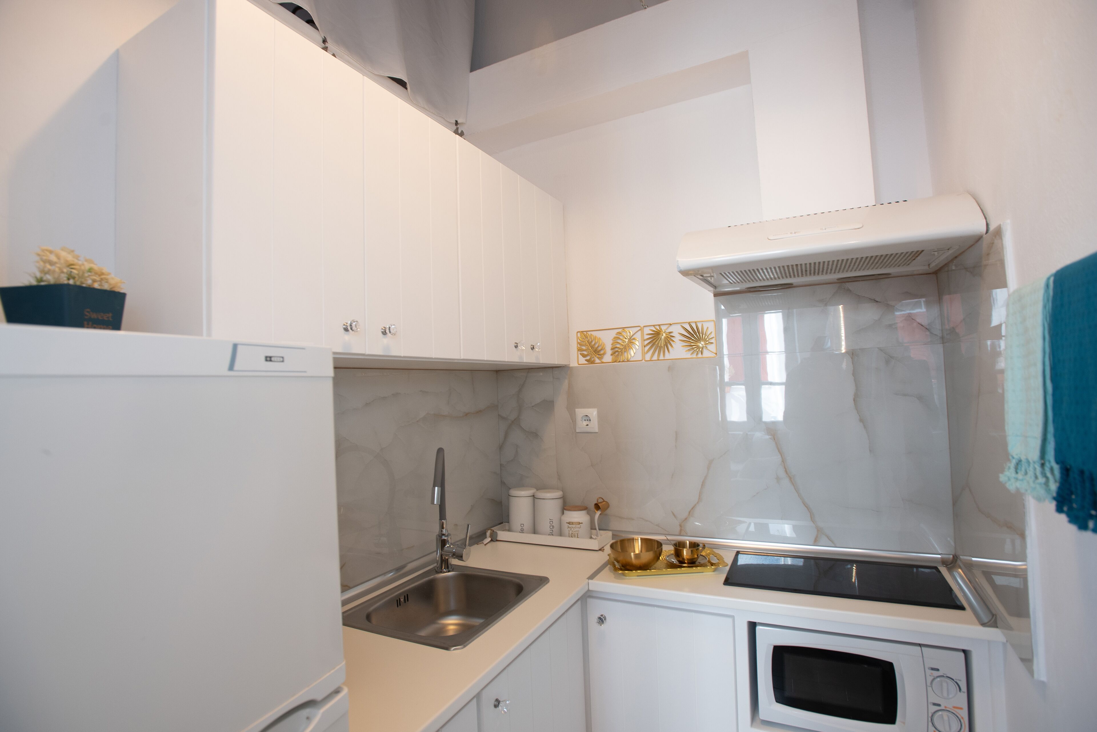 A compact kitchen with white cabinets, a built-in microwave, a stainless steel sink, and a decorative backsplash.