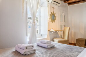 A hotel room with a bed, a chair, a small table, and a window with curtains. - Seablue Town Maisonette (Mykonos)