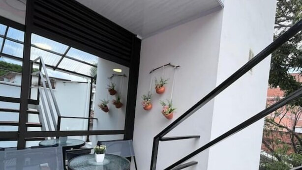 Un balcon moderne avec une table et des chaises en verre, des plantes en pot et une rambarde en métal.