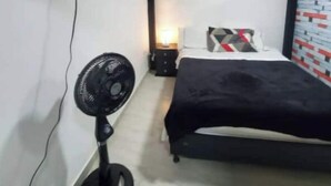 Une chambre à coucher avec un lit, un téléviseur fixé au mur et un ventilateur sur pied.