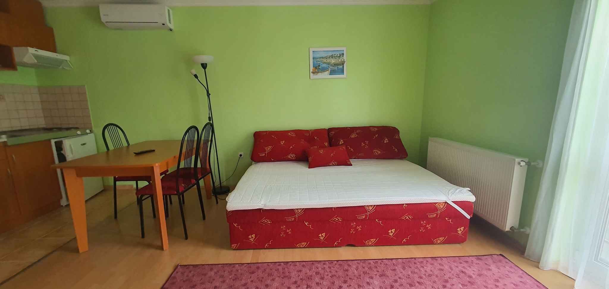 A room with a bed, a table, chairs, a radiator, and a picture on the wall.