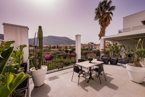Eine Terrasse mit Tisch und Stühlen, umgeben von Kübelpflanzen und Blumen, mit Blick auf eine Wohngegend und dahinter Bergen.