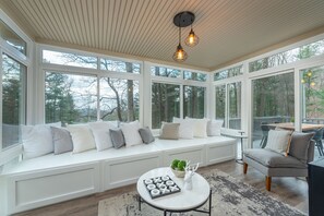 A sunroom with a built-in bench, large windows, and a round table with a board game. - Ashevilles Beautiful Home (Arden)