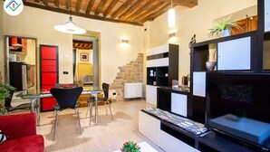 A modern kitchen with a built-in oven, a dining area with a red chair, and a TV on a black stand. - Antica Piazza Apartment (Lucca)