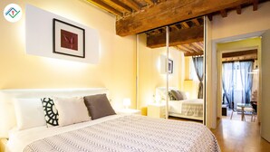 A hotel room with a large bed, a bedside table with a lamp, a framed picture on the wall, and a sliding door leading to a balcony. - Antica Piazza Apartment (Lucca)