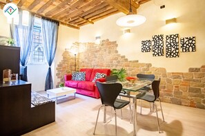 A cozy living area with a red sofa, a glass dining table, and a stone wall. - Antica Piazza Apartment (Lucca)