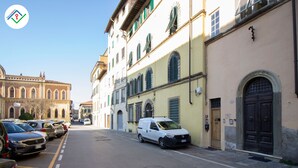 A street with parked cars and a white van, buildings with arched windows and doors, and a clear sky. - Antica Piazza Apartment (Lucca)