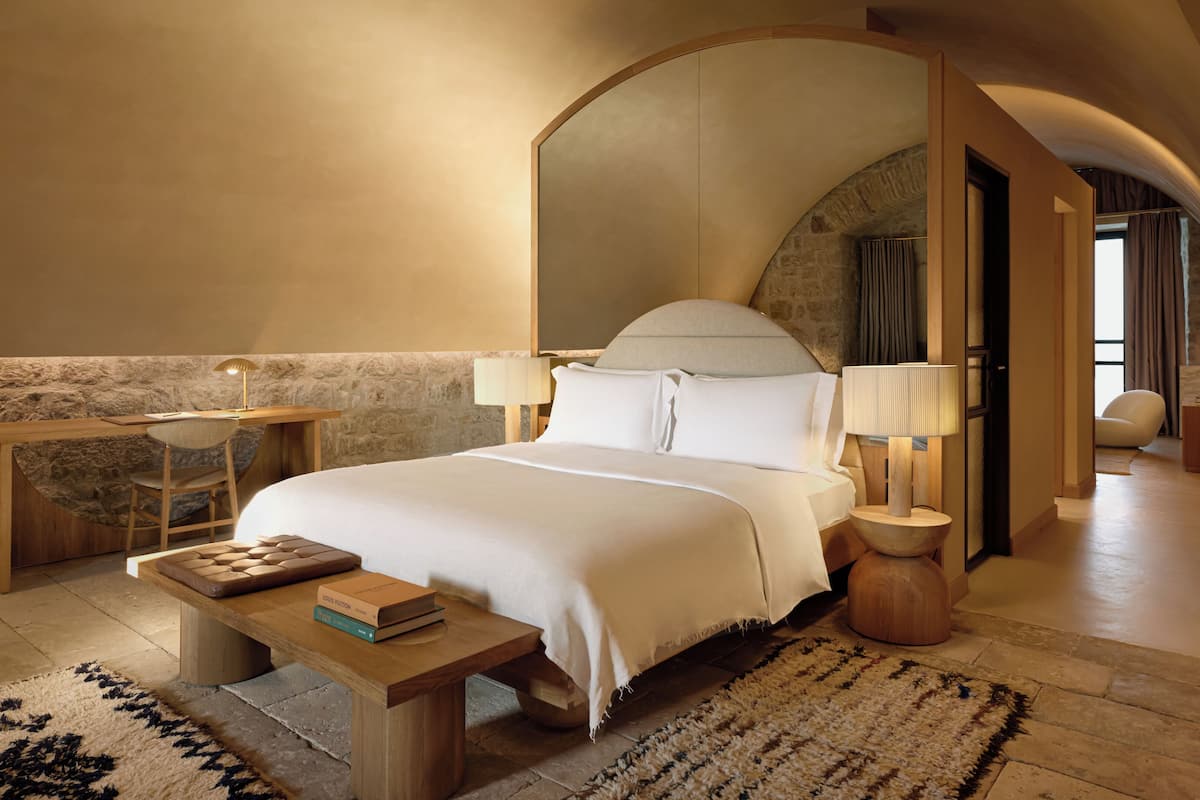 A modern hotel room with a large bed, a wooden desk, and a reading chair.
