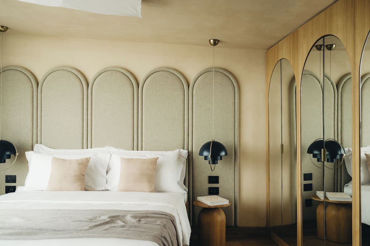 A bedroom with a bed, bedside lamps, a mirror, and a wooden floor.