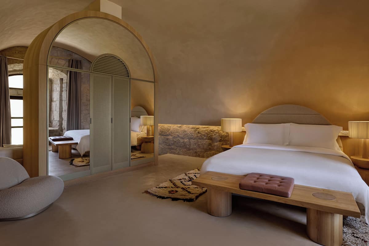 A bedroom with a large bed, a wooden nightstand, a bedside table, a chair, and a mirror.