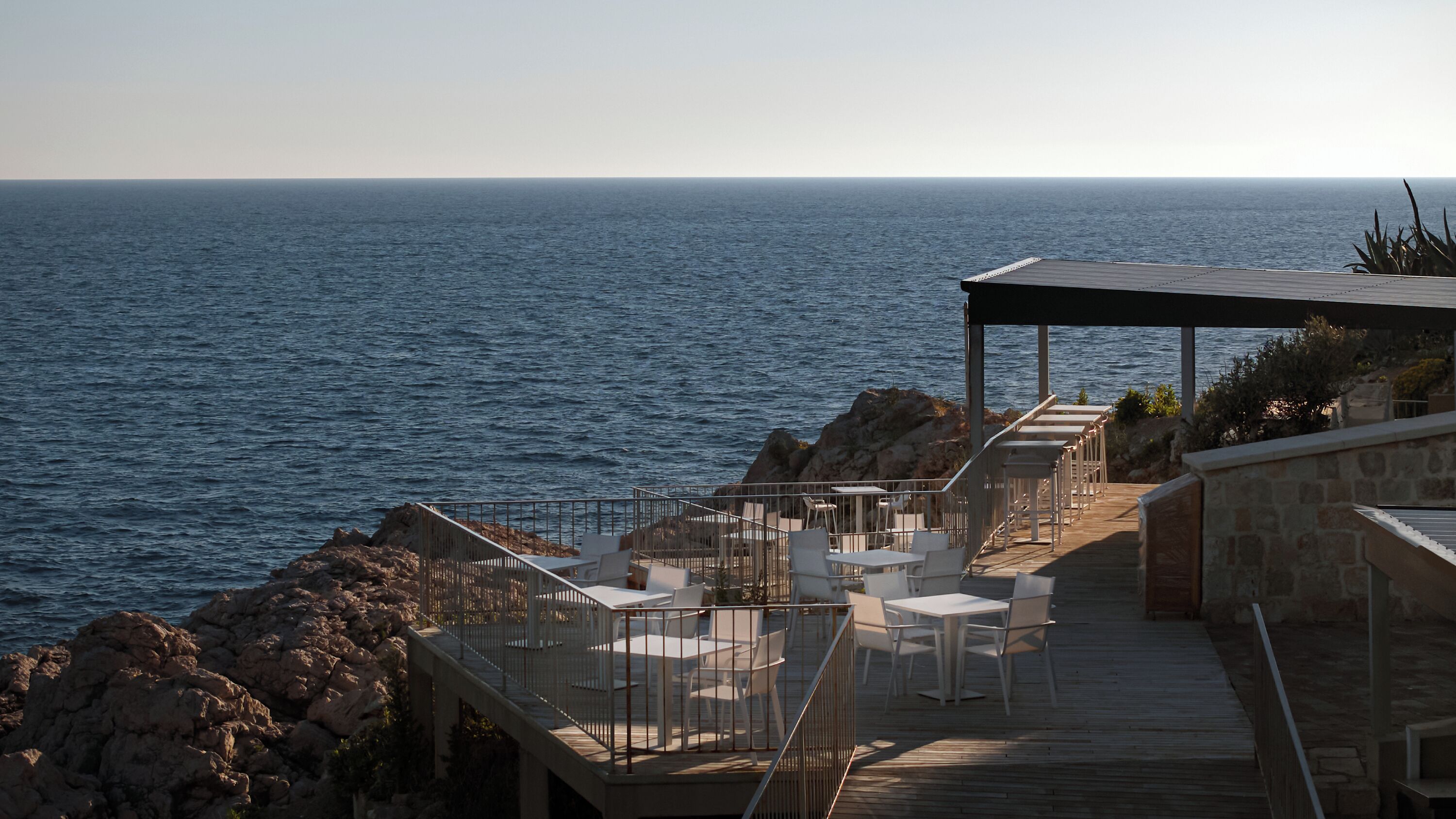 Un restaurante frente al mar con terraza al aire libre, paredes de piedra y una cubierta de madera.
