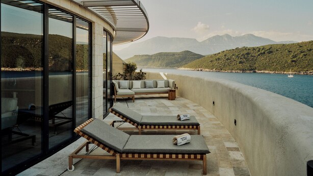 A balcony with lounge chairs, a sofa, and a view of a body of water and mountains. - Mamula Island by Banyan Tree (Mamula Island)
