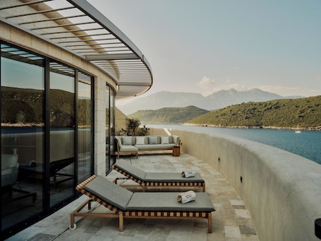 A balcony with lounge chairs, a sofa, and a view of a body of water and mountains.