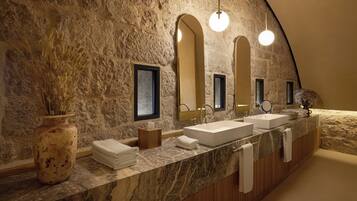 A bathroom with a stone wall, a marble countertop, two sinks, and a large mirror.