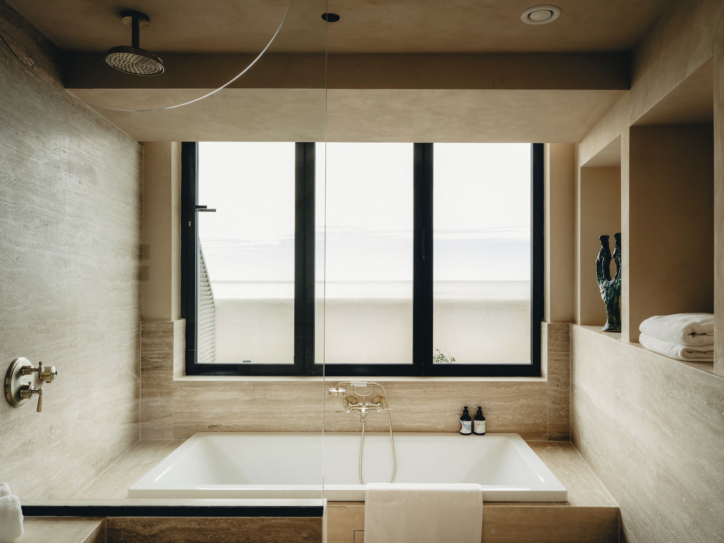 Un baño moderno con una bañera grande, una ventana con vistas a la playa y un cabezal de ducha.