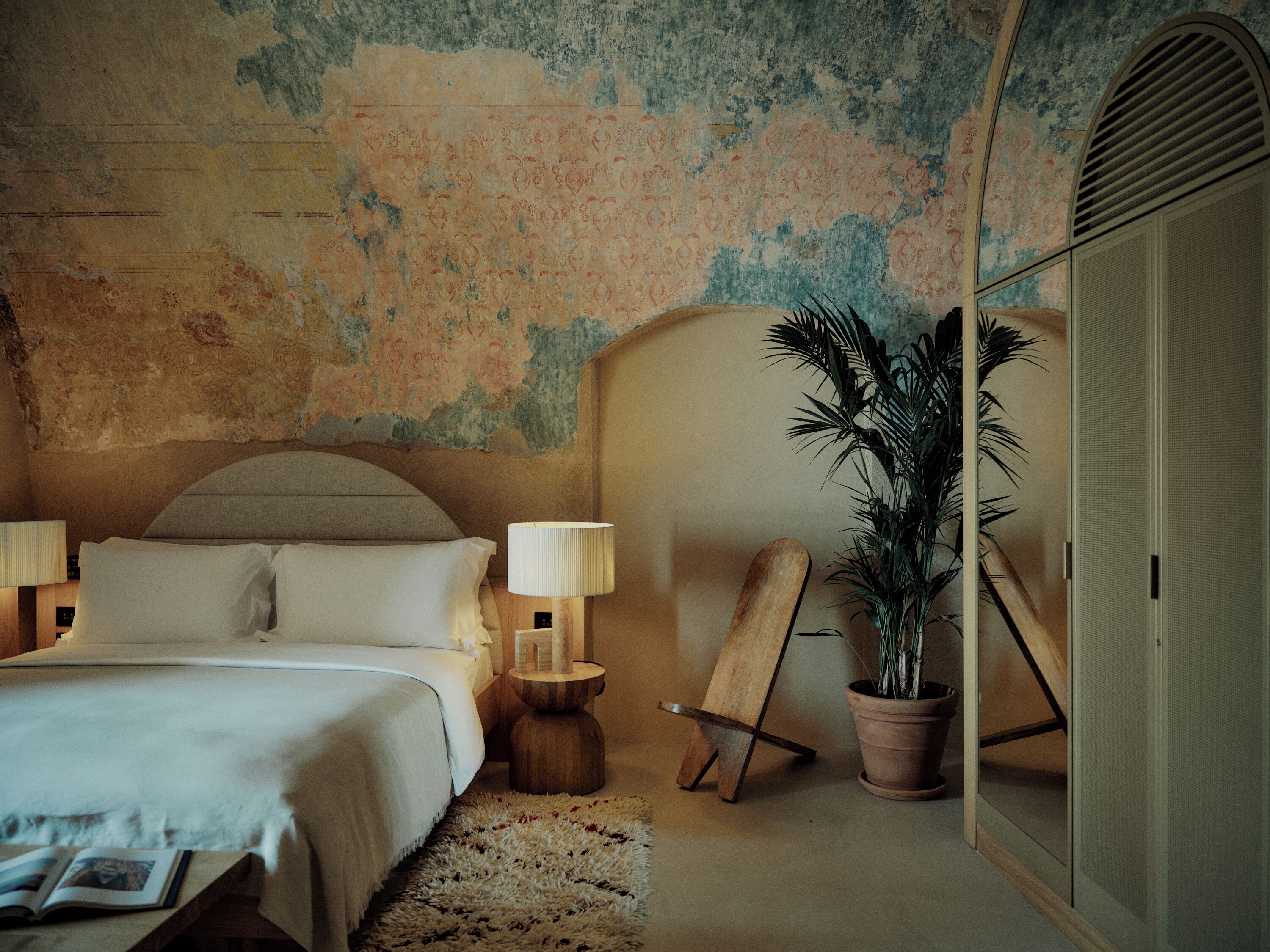 A bedroom with a bed, bedside lamps, a wooden sideboard, a potted plant, and a wardrobe.
