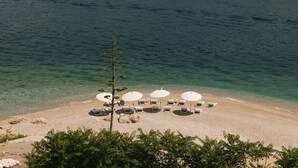 A beach with clear water, white umbrellas, and lounge chairs arranged on the sand. - Mamula Island by Banyan Tree (Mamula Island)