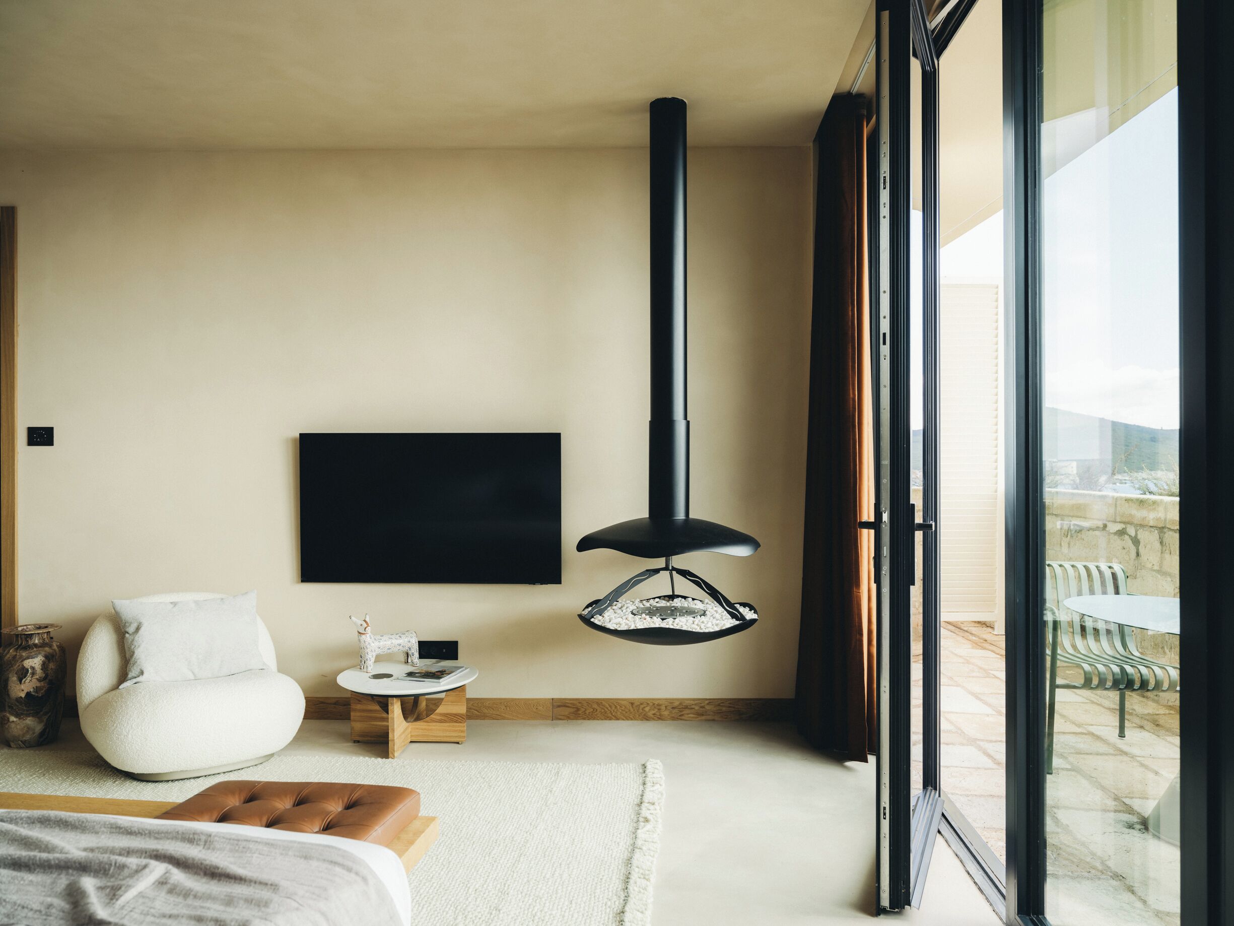 A modern bedroom with a large window, a flat-screen TV, a fireplace, a sofa, and a small table.