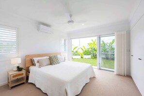 Une chambre à coucher comprenant un lit, une table de chevet, une lampe et donnant sur un jardin grâce à une porte-fenêtre coulissante.