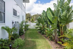 Un bâtiment blanc avec un chemin pavé, entouré d’une végétation luxuriante et d’une clôture blanche.