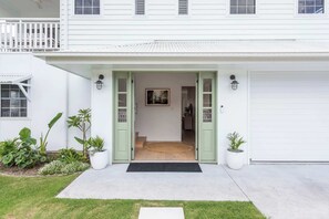 A white house with a front porch, potted plants, and a door leading to the interior.
