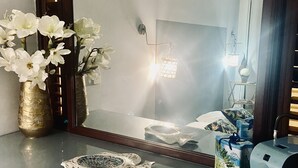 Un lavabo con specchio, un vaso di fiori bianchi, un piatto decorativo, una lampada e una macchina da caffè.