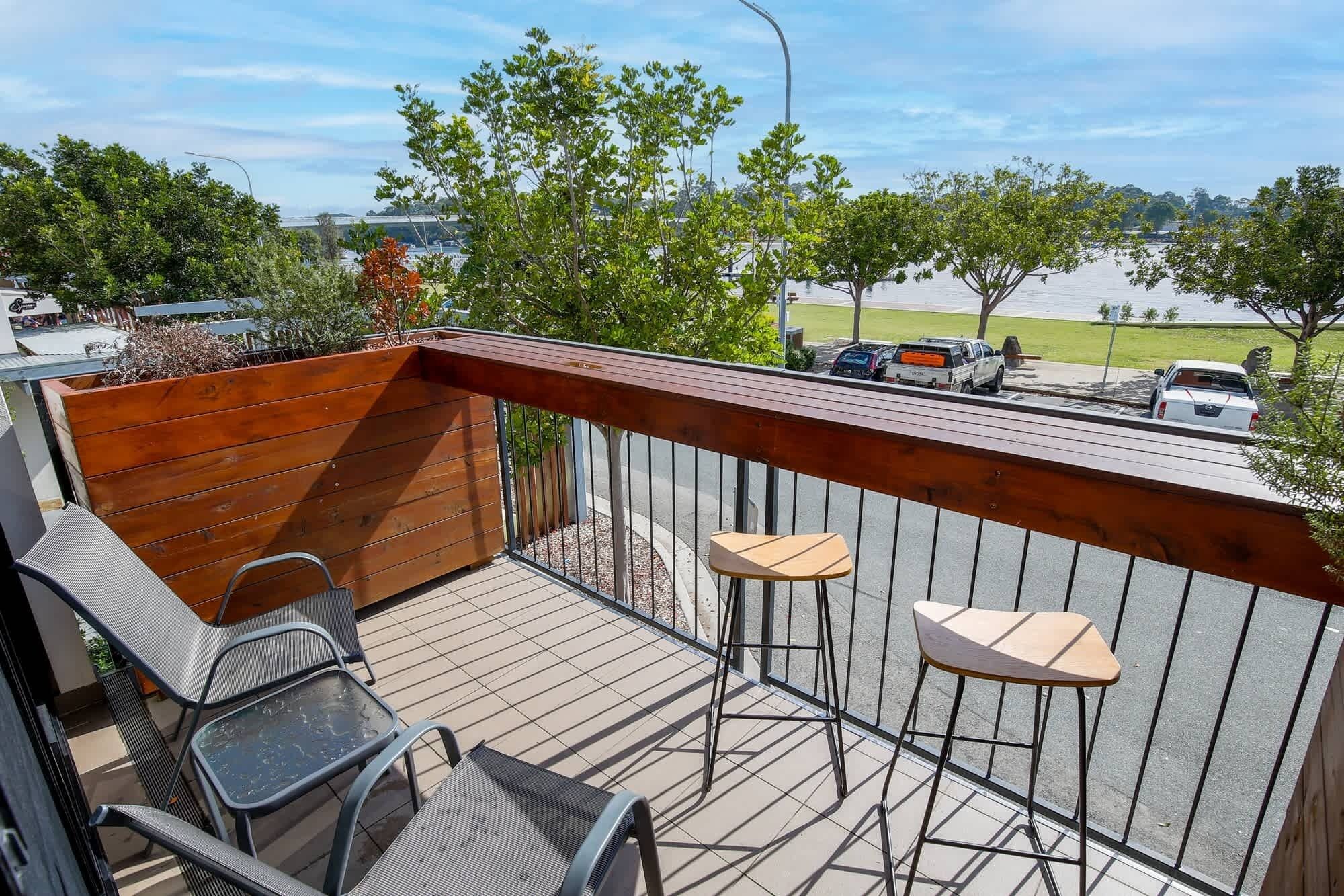 Een balkon met een houten terras, metalen stoelen en een kleine tafel.