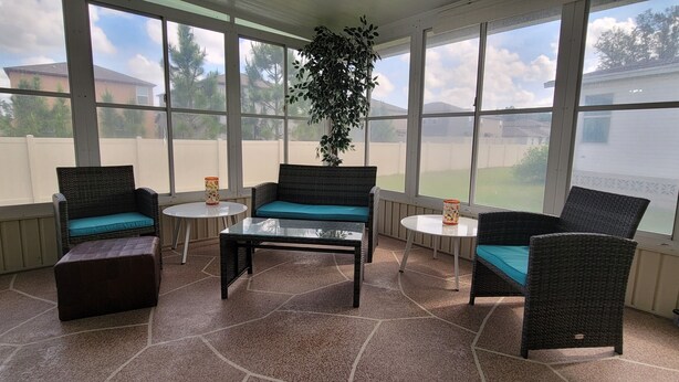A covered patio area with wicker furniture, a glass table, and a potted plant.