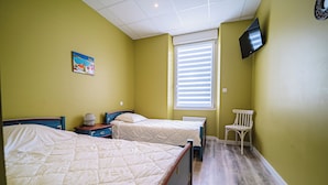 Une chambre avec deux lits, une fenêtre avec des stores, un téléviseur fixé au mur et une chaise.