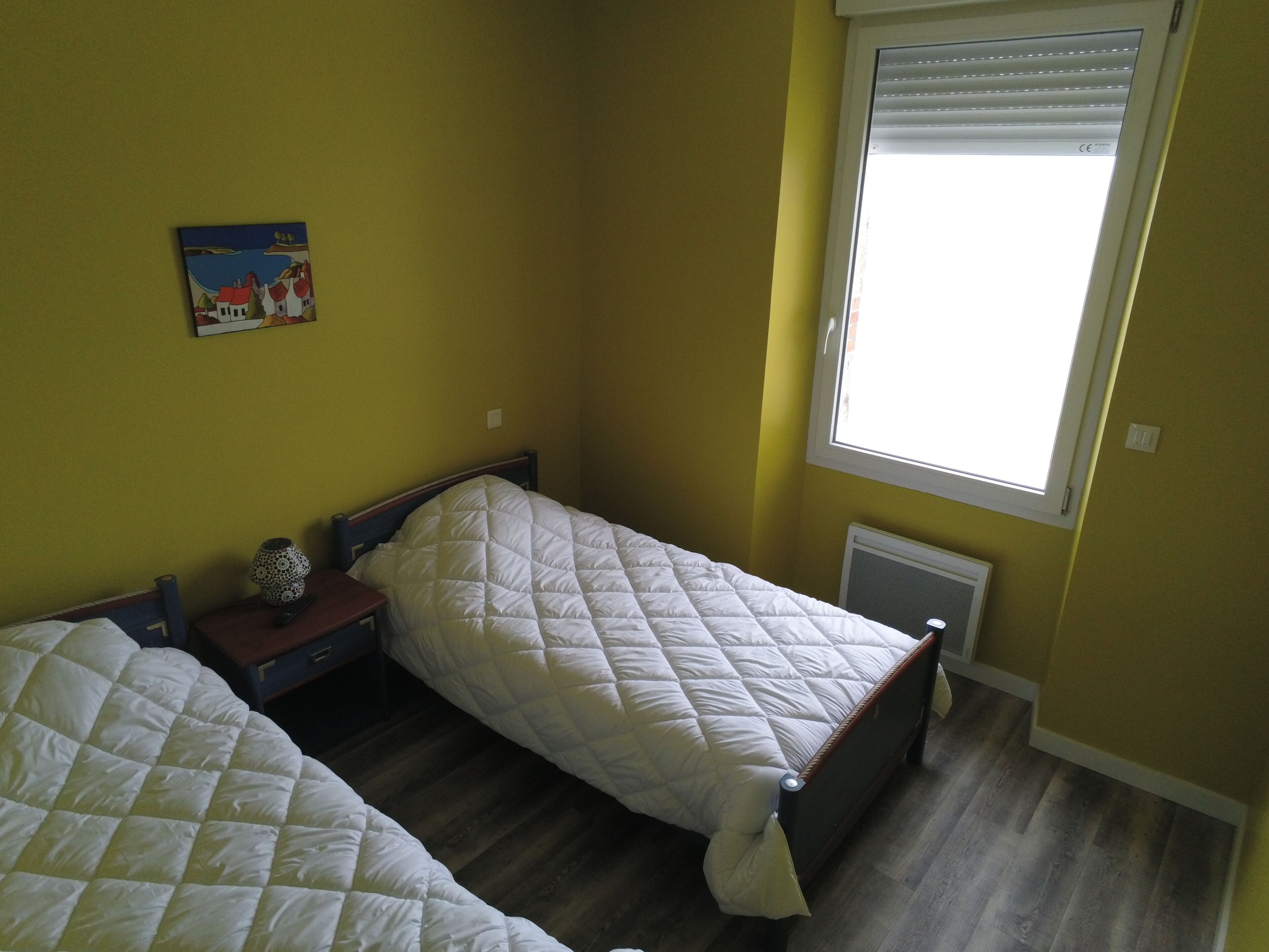 A bedroom with two beds, a window, and a painting on the wall.