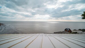 Une vue depuis le toit d’un bâtiment, dont le toit est en métal, donnant sur une plage et la mer.