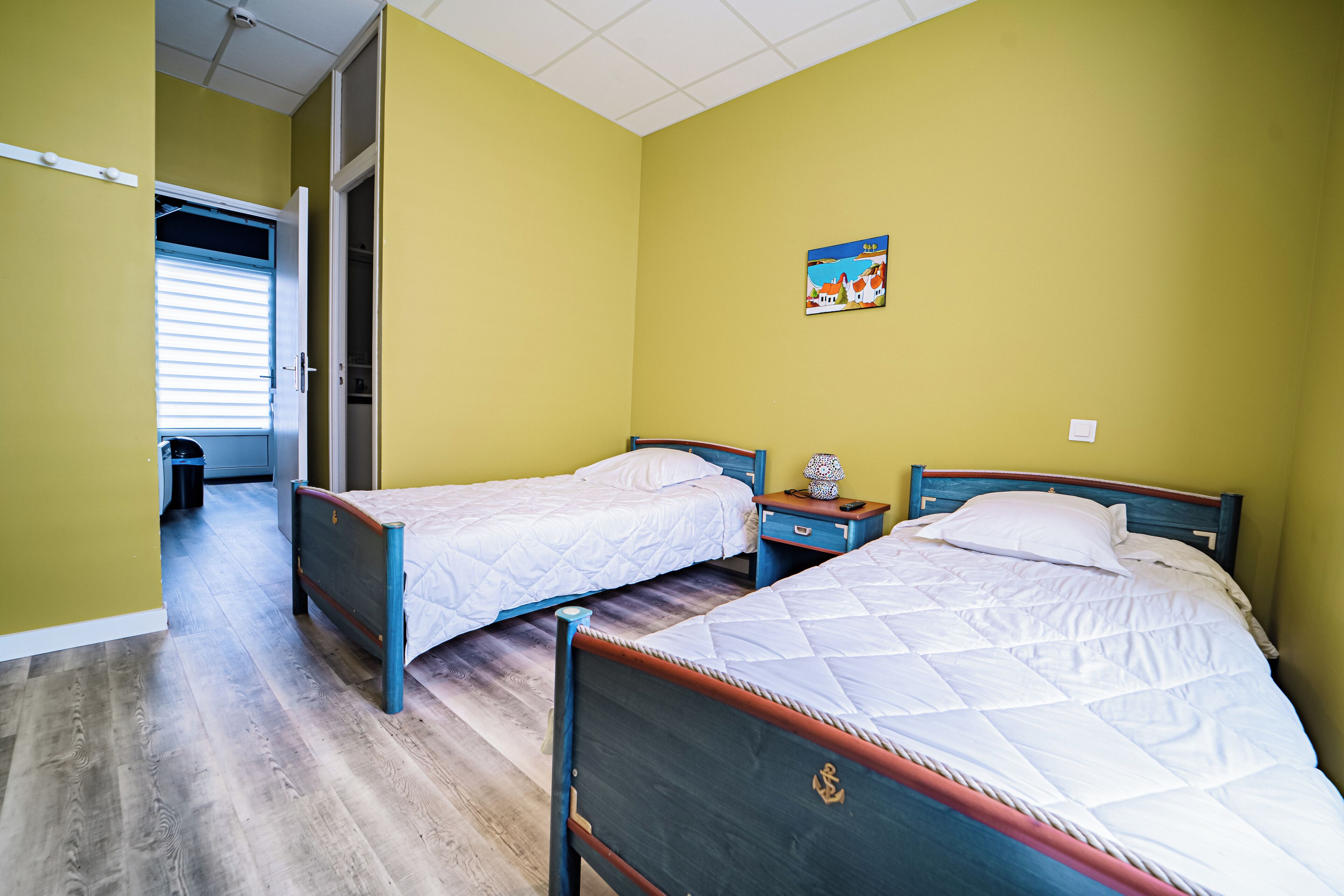 Een kamer met twee bedden, houten hoofdborden, een klein nachtkastje met een lamp, en een schilderij aan de muur.