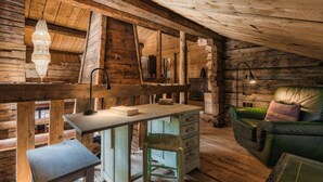A rustic cabin interior with a wooden desk, a chair, a sofa, and a lamp.