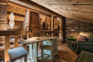 A rustic cabin interior with a wooden desk, a chair, a sofa, and a lamp.