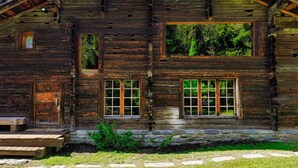 A rustic log cabin with a stone foundation, large windows, and a wooden porch.