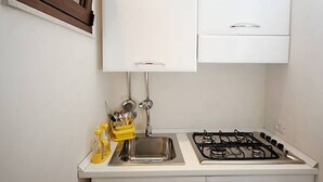 A small kitchen with a gas stove, a sink, and a cabinet above the sink. - Fisherman's House (Trapani)