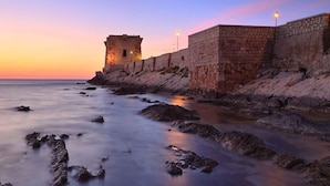 A coastal stone wall with a tower and a stone building, overlooking a rocky shoreline. - Fisherman's House (Trapani)