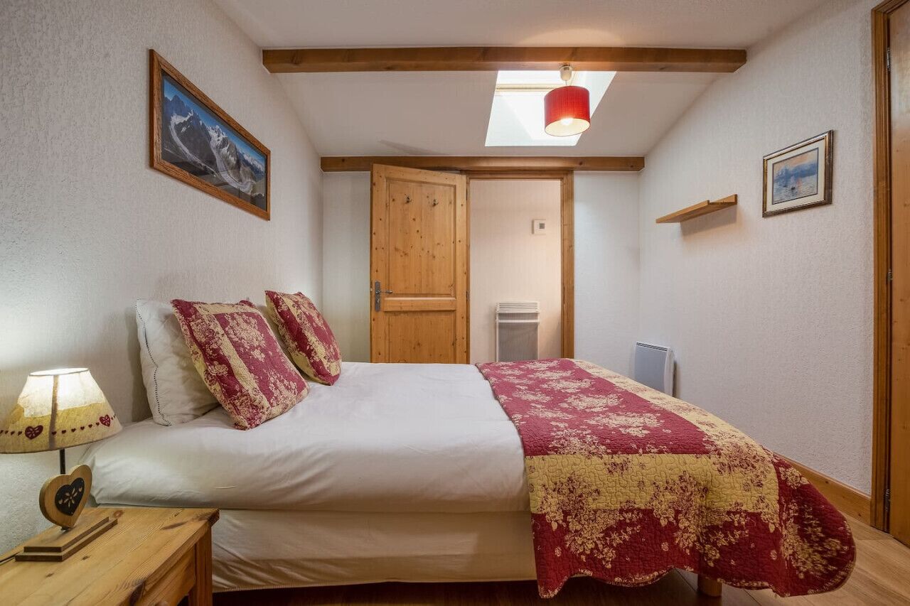 A bedroom with a bed, a nightstand, a lamp, a heater, a door, and a skylight.