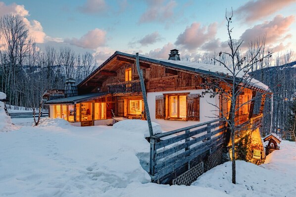 A wooden cabin with a balcony, surrounded by snow and trees.