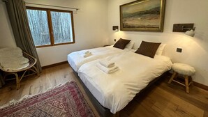 Ein Schlafzimmer mit zwei Betten, einem großen Fenster, einem Sessel und einem Teppich.
