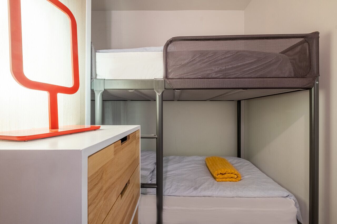 A bunk bed with a desk and drawers, a window with a red frame, and a yellow towel on the lower bunk.