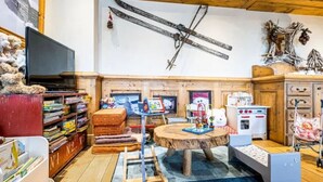 Una habitación acogedora con techo de madera, televisor, estantería, una mesa redonda y una cuna.