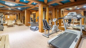 Un gimnasio con equipamiento de ejercicio, vigas de madera y un techo con tragaluces.