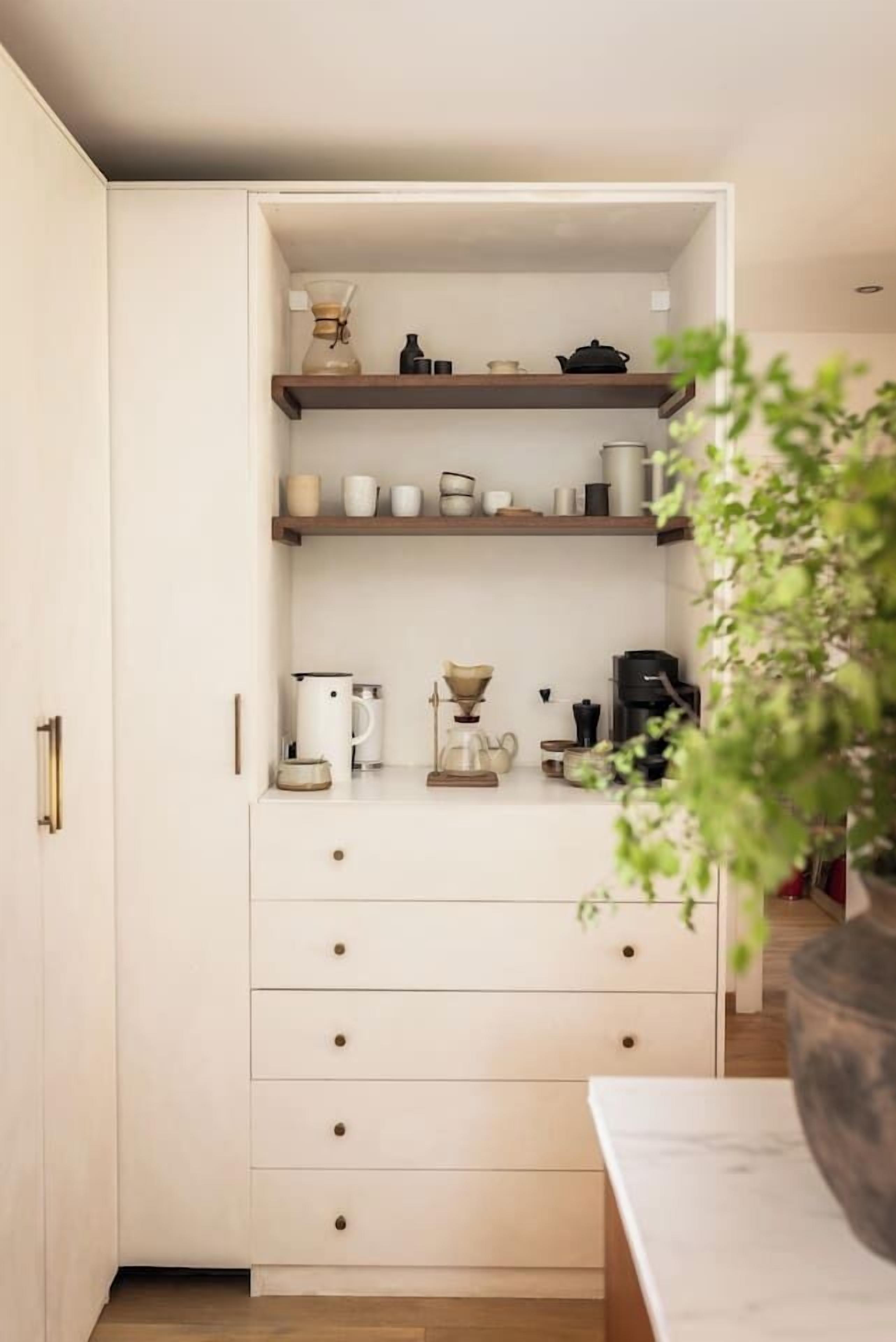 Una cocina con armarios blancos, repisas de madera y diversos electrodomésticos.