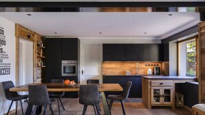 Une cuisine moderne avec des meubles de couleur sombre, un îlot central et un coin repas comprenant une table et des chaises en bois.
