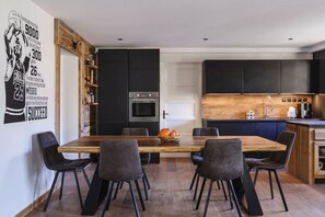 Una cocina moderna con armarios oscuros, una isla central y una zona de comedor con una mesa y sillas de madera.