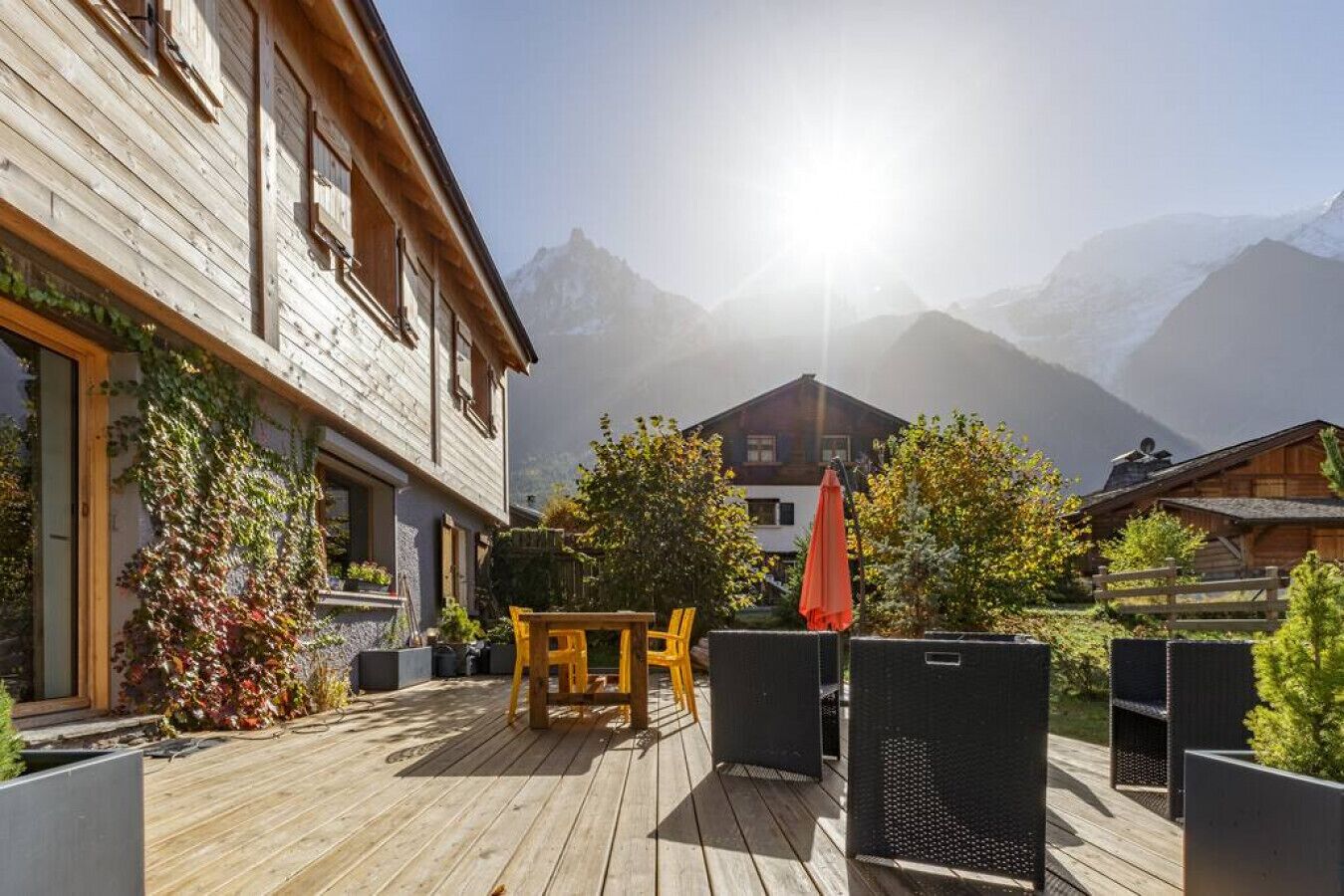 A wooden deck with outdoor furniture, a mountain view, and a building with a sloped roof.