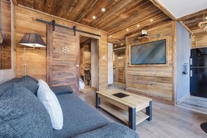 A cozy cabin interior with a sofa, a table, a TV, and a wooden ceiling.
