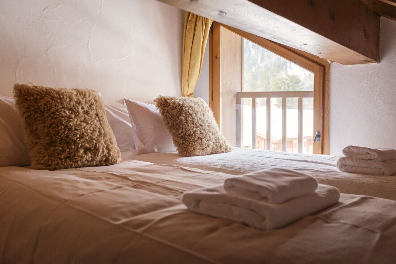 Une chambre confortable avec une grande fenêtre, un plafond en bois et des serviettes soigneusement pliées sur le lit.