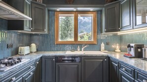 Una cocina con armarios oscuros, un lavamanos doble, una estufa y una ventana con vistas a árboles y una casa.